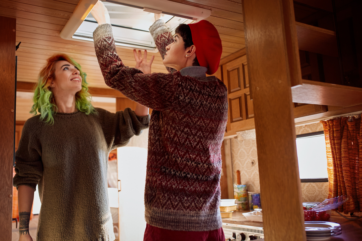Two friends fixing roof window inside of camper trailer.