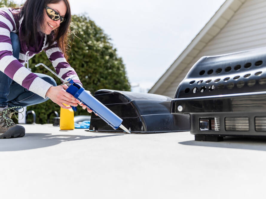 Woman Doing Maintenance of Camper Trailer. She is applying a sealant around the windows and other parts of the trailer. The seasonal maintenance of a travel trailer, a caravan, a motor home or a camper trailer is very important to enjoy the camping season.
