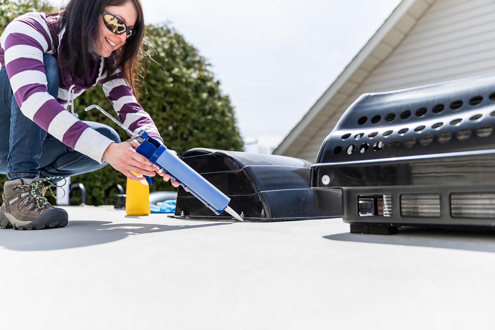 Woman Doing Maintenance of Camper Trailer. She is applying a sealant around the windows and other parts of the trailer. The seasonal maintenance of a travel trailer, a caravan, a motor home or a camper trailer is very important to enjoy the camping season.
