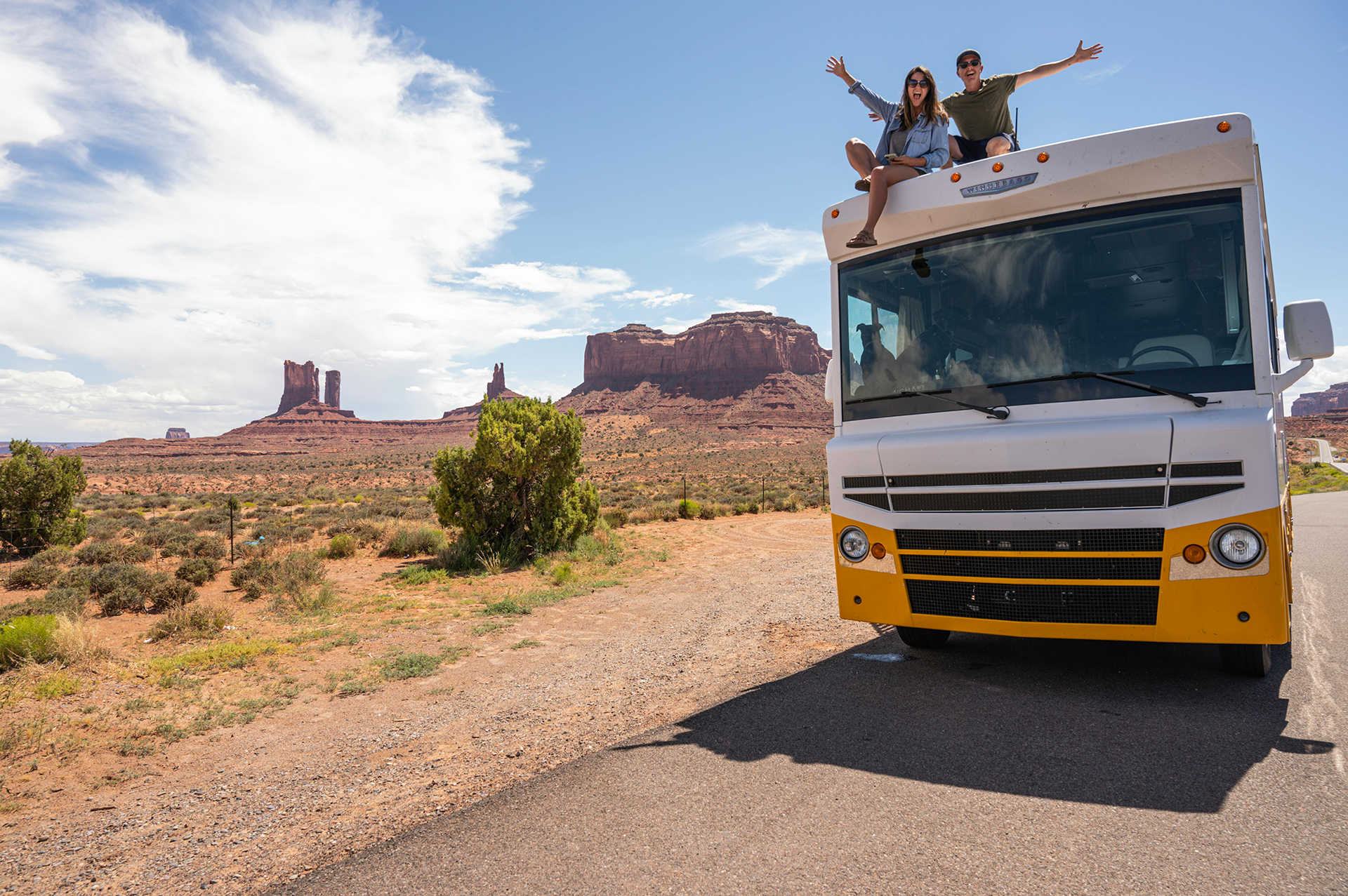 Young couple on top of RV celebrating a road trip.